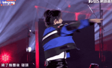 a woman in a blue and black jacket is dancing on a stage with a tvbs logo in the background