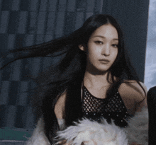 a woman with long black hair wearing a black top and a white fur coat