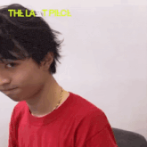 a young man wearing a red t-shirt and a gold necklace is looking at the camera .