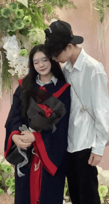a girl in a graduation gown is holding a bouquet of flowers while a man kisses her on the forehead
