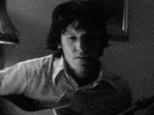 a man in a white shirt is playing a guitar in a black and white photo