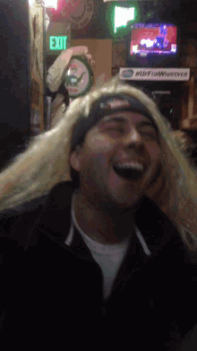 a man with long blonde hair is laughing in front of a green exit sign