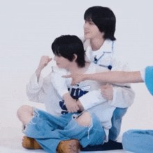 a couple of young men are sitting on the floor and one of them is pointing at the other .