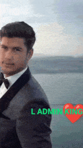 a man in a tuxedo and bow tie is standing in front of a body of water ..