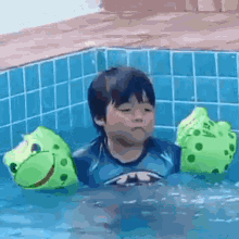 a young boy is swimming in a pool with frog floaties on his arms