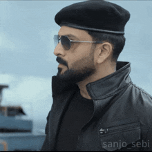 a man with a beard wearing sunglasses and a beret with the name sanjo sebi on the back of his jacket