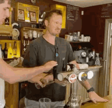 a man is pouring beer into a glass while another man stands behind him .