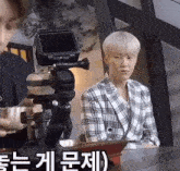 a man in a plaid jacket is sitting at a table in front of a video camera .