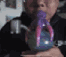 a man is blowing a purple balloon into a glass .