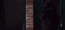 a man is standing in front of a door in a dark room with a brick wall .