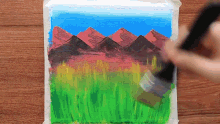 a person is painting a picture of mountains and grass with a brush