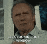 a man is standing in front of a window and looking out of it .
