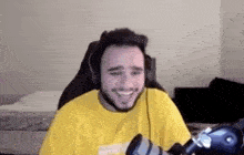a man wearing headphones and a yellow shirt is smiling while sitting in a chair .