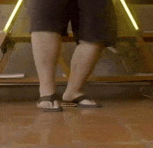 a person wearing flip flops is standing on a wooden floor .