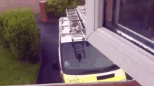a yellow van with a ladder on the roof is parked in front of a window .