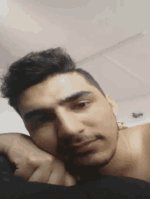 a man without a shirt is laying on a bed with his head resting on his hand