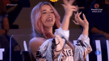 a woman with pink hair is applauding in front of a sign that says masterchef
