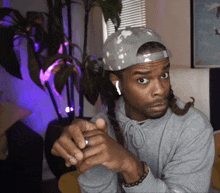 a man with dreadlocks wearing a hat and a gray hoodie
