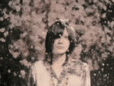 a woman is standing in front of a tree with flowers falling on her face .