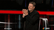a man applauds in front of a screen that says the voice