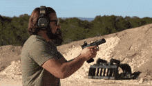 a man wearing ear muffs holds a gun in his right hand