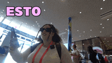 a woman wearing sunglasses and a lanyard stands in front of a sign that says esto