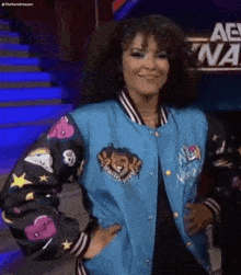 a woman wearing a blue bomber jacket with a lion on the sleeves is smiling .