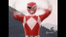 a red power ranger is standing in front of a mountain with his hands in the air .