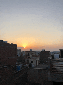 a sunset over a city with a few buildings and water tanks in the foreground