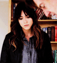 a woman in a black jacket is standing in front of a bookshelf ..