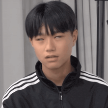 a young man wearing a black jacket with white stripes on the sleeves is making a funny face