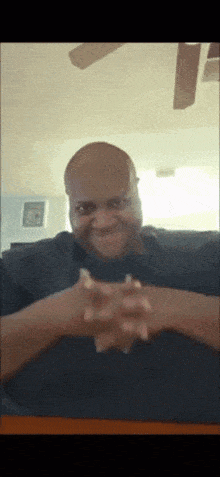 a bald man is sitting at a table with his hands folded in front of his face