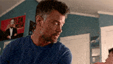 a man in a blue shirt is sitting in front of a elon musk poster .