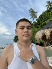 a man in a white tank top is wearing a watch and giving the peace sign