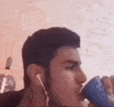 a man is drinking from a can while wearing ear buds .