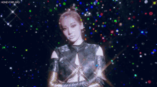 a woman in a black top and gold gloves stands in front of a colorful background