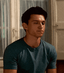a man in a blue t-shirt is sitting in front of a window .