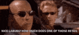 two men wearing sunglasses are driving a car and one of them is talking to the other .