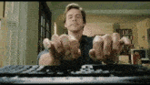 a man is sitting at a keyboard with his hands up .