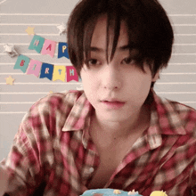 a young man in a plaid shirt is holding a birthday cake