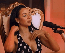 a woman in a black and white polka dot dress is sitting in a chair in front of a microphone