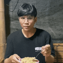 a man wearing glasses and a black shirt that says pete 's pizza is eating food