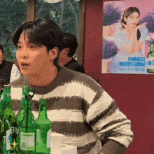 a man in a striped sweater is sitting at a table with green bottles of beer