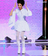 a woman in a white dress and white boots is dancing on a stage with t4yce tumblr in the background