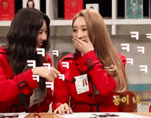 two girls in red coats are laughing and one has a name tag on her neck