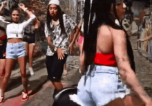 a group of people are dancing on a street in front of a graffiti wall .