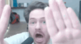 a man with a beard is making a funny face with his hands outstretched .