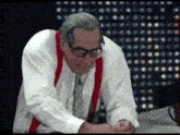 a man in a white shirt and red suspenders looks down