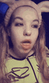 a girl wearing bunny ears and a pink headband is making a face .