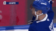 a hockey player wearing a blue helmet holds a hockey stick in front of a sn logo